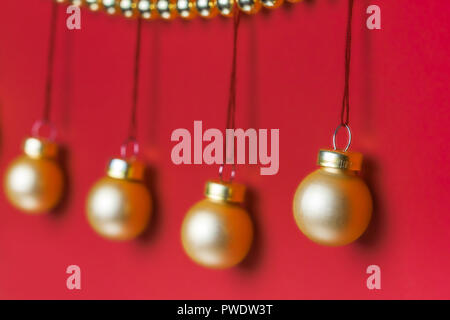 Fünf kleine matt Gold-farbigen Christmas ornament hängend an einer Reihe von glänzenden goldenen - farbige Weihnachten Perlen dekoriert Kranz auf rotem Hintergrund in St Stockfoto