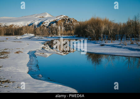 Snowy Mongolische Landschaft, Reflexion der schneebedeckten Berge, Bäume und blauer Himmel in einem eisigen Fluss. Arkhangai, Mongolei Stockfoto