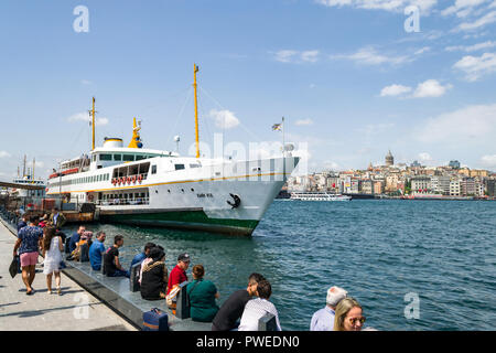 Man saß auf Stein sitzen von Eminonu Pier mit Fähre im Hintergrund angedockt, Istanbul, Türkei Stockfoto