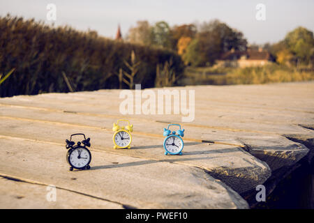 Drei kleine Alarm retro Uhren auf Holz- Oberfläche. Herbst abstrakten Foto. Sommerzeit. Stockfoto