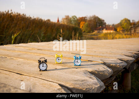 Drei kleine Alarm retro Uhren auf Holz- Oberfläche. Herbst abstrakten Foto. Sommerzeit. Stockfoto