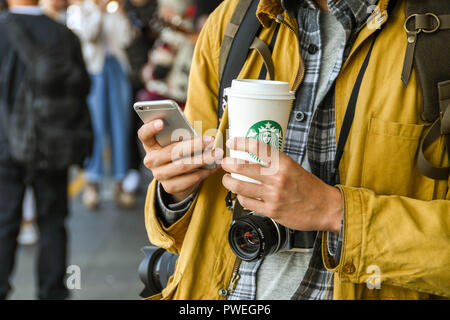 SEATTLE, WASHINGTON STATE, USA – JUNI 2018: Nahaufnahme eines Touristen mit einer Kamera, die SMS auf einem Telefon sendet und eine Tasse Starbucks-Kaffee in der Hand hält Stockfoto