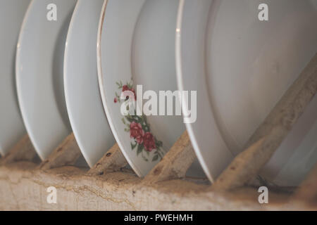 Alte Porzellanteller mit Blumenschmuck in Holzregal Stockfoto