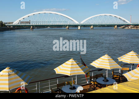 Serbien, in Novi Sad an der Donau, Provinz Vojvodina, Bezirk Süd Backa, Flusskreuzfahrt auf der Donau, Ausflug Schiff, offenen Achterdeck auf dem Cruiser aROSA Mia, Sonnenschirme, Tourismus, Donau Navigation, Blick auf zwei Donaubrücken, Straßen-, Brücken- und Eisenbahnbrücken, hinter der Brücke, die meisten Zezeljev Zezelj, vor der Brücke, Bosko Perosevic Road-Railway Brücke, Die meisten boska Perosevica, der Europäischen Kulturhauptstadt 2021 Stockfoto