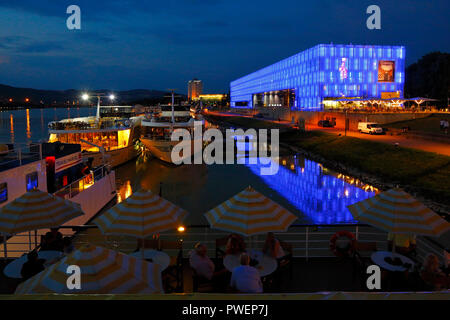 Österreich, Oberösterreich, Linz an der Donau, Landeshauptstadt von Oberösterreich, Kulturhauptstadt 2009, Nacht Foto, Abendstimmung, Donau Kreuzfahrt, Sonnenschirme, Touristen auf dem Achterdeck des Kreuzers aROSA Mia, die Ausflugsschiffe an der Schiffsanlegestelle Donaulaende, rechts das Lentos Kunstmuseum, im Hintergrund das Hotel Arcotel Linz Stockfoto