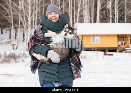 Taille bis Porträt der moderne junge Frau lächelnd in die Kamera halten cute Husky Welpen im Winter, kopieren Raum Stockfoto