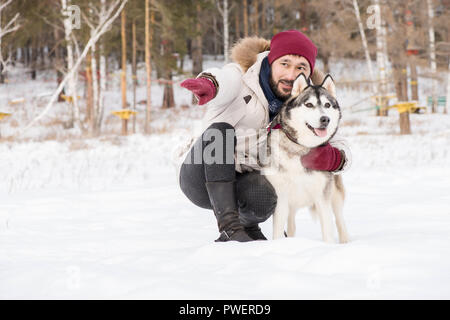 In voller Länge Porträt des modernen asiatischen Mann liebevoll im Gespräch mit wunderschönen Husky Hund während sie Zeit im Freien im Winter, kopieren Raum Stockfoto