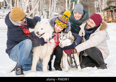 In voller Länge Porträt von zwei Paare spielen mit zwei schönen Hunde im Winter Resort, kopieren Raum Stockfoto