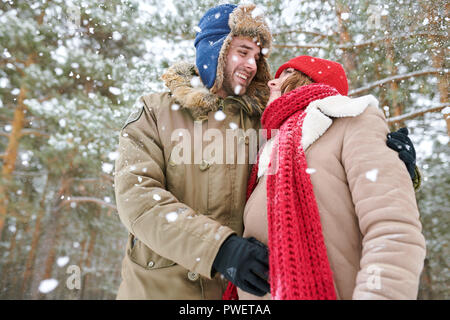 Taille bis Portrait von liebevolle junge Paar zärtlich und Suchen umarmen einander an, während im verschneiten Winterwald Posing, kopieren Raum Stockfoto