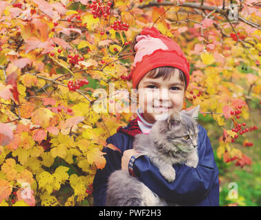 Kleines Mädchen umarmt eine Katze im Garten im Herbst Stockfoto