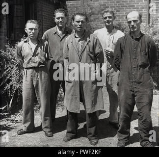 1950er Jahre, Gruppe von britischen reifen Fabrikarbeiter in ihre Arbeit Kleidung oder Overalls stehen außerhalb der Firma Büro für ein Bild, England, UK. Stockfoto