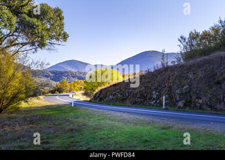 Landstraße zwischen Hügeln und Bäumen in die schöne Landschaft bei Sonnenuntergang Biegen Stockfoto