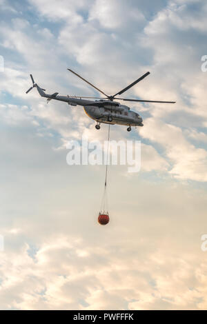 Ein Feuerwehrmann Hubschrauber mit einem vollen Korb von Wasser fliegt gegen einen schönen Himmel Stockfoto