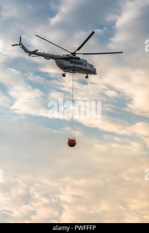 Ein Feuerwehrmann Hubschrauber mit einem vollen Korb von Wasser fliegt gegen einen schönen Himmel Stockfoto