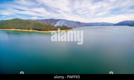 Antenne Panorama der aufsteigenden Rauch aus Wald inmitten von wunderschönen malerischen Hügeln auf dem Lake Shore Stockfoto