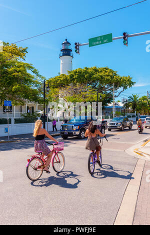 Straße mit Autos und Radfahrern in Key West, Florida Keys, Florida, USA. Der berühmte Key West Leuchtturm kann auch gesehen werden. Stockfoto