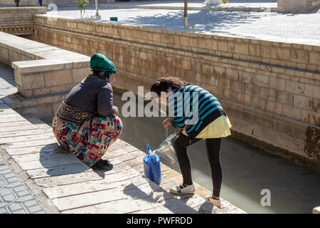 Buchara, Usbekistan - September 22, 2018: Frauen Zeichnung Wasser von Canal central square in Buchara, Usbekistan zu reinigen. Stockfoto