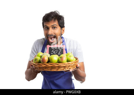 Fröhliche indischen Lebensmittelladen Mitarbeiter präsentieren 50 Prozent Rabatt im frische Äpfel in einem Korb mit sehr positiven Ausdruck isoliert auf weißem Stockfoto