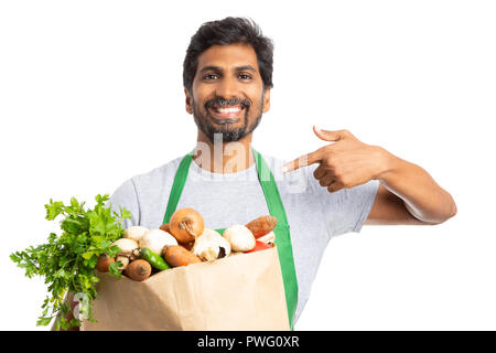 Lächelnd Lebensmittelgeschäft oder Supermarkt Mitarbeiter präsentieren frische Produkte in Papier Beutel mit Zeigefinger isoliert auf weißem Stockfoto