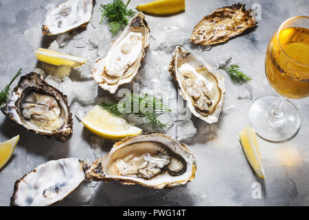 Geöffnete Austern und Glas Weisswein auf grauem Beton Texturen Hintergrund. Stockfoto