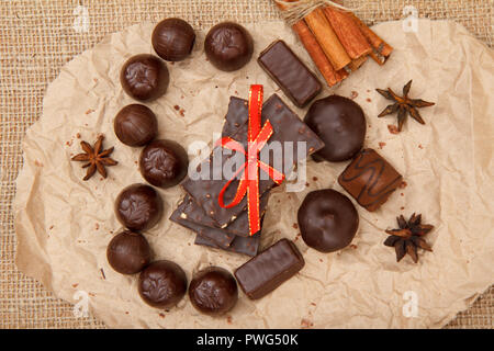 Schokolade Süßigkeiten verschiedene Form und Schokoriegel mit Muttern auf Stück pack Papier in Form von einem Herz mit Sternen Anis und Zimt. Ansicht von oben Stockfoto