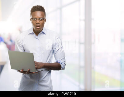 Junge afrikanische amerikanische Geschäftsmann mit Computer laptop Angst im Schlag mit einer Überraschung konfrontiert, ängstlich und aufgeregt mit Angst Ausdruck Stockfoto