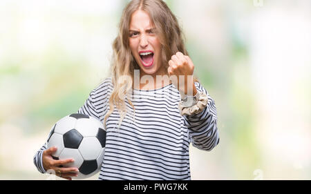 Schöne, junge blonde Frau mit Fußball-Fußball-Kugel über isolierte Hintergrund genervt und frustriert schrie mit Zorn, verrückt und mit Schreien Stockfoto