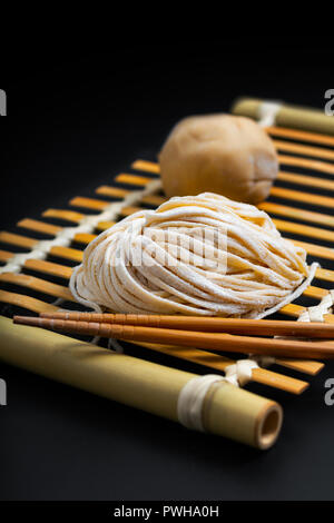 Essen frische rohe Hausgemachte orientalische asiatische, chinesische Eiernudeln durch organische Eier und Mehl halbweiss auf einem Bambus Fach Stockfoto