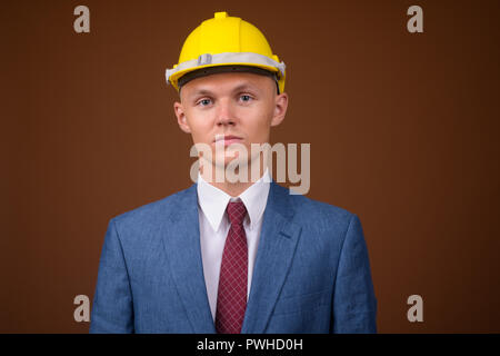 Junge Unternehmer tragen, hardhat gegen braunen Hintergrund Stockfoto