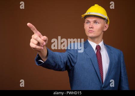 Junge Unternehmer tragen, hardhat gegen braunen Hintergrund Stockfoto