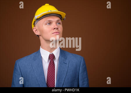 Junge Unternehmer tragen, hardhat gegen braunen Hintergrund Stockfoto