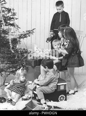 Weihnachten in den 60er Jahren. Kinder in verschiedene Altersgruppen in einem Raum mit am Weihnachtsbaum und Geschenke. Einige präsentiert wurde geöffnet, und die Kinder sind mit Ihnen zu spielen. Schweden 1965 Stockfoto