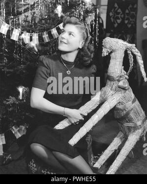 Weihnachten in den 1940er Jahren. Die jungen Eiskunstlauf Britta Råhlen feiert Weihnachten zu Hause in den 1940er Jahren. Sie hält eine traditionelle Stroh Ziege, als sie durch den Weihnachtsbaum sitzt. Schweden 1940. Stockfoto