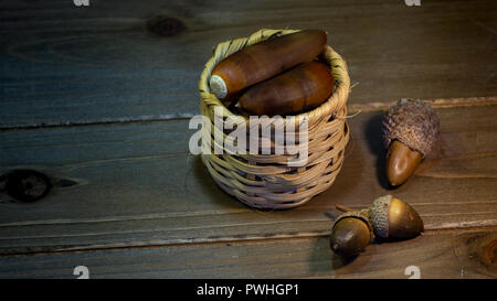 Sortierte Eicheln aus Kalifornien in einem kleinen Korb und auf Holztisch - Herbst noch leben Zusammensetzung Stockfoto