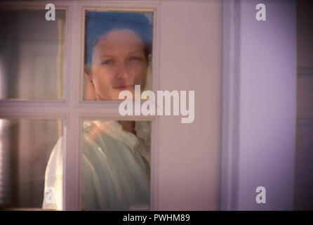 Eine schöne junge Frau auf der Suche durch das Fenster. Stockfoto