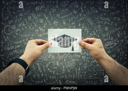 Nahaufnahme des Menschen Hände innen halten Sie ein weißes Blatt Papier mit akademischen cap Symbol über die Kreide geschrieben Tafel Hintergrund. Pädagogisches Konzept, Col Stockfoto