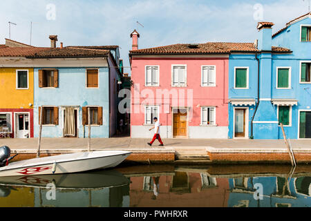 Ein Mann der Vergangenheit eine Reihe von bunten Häusern durch den Kanal in Burano, Venedig, Italien Stockfoto