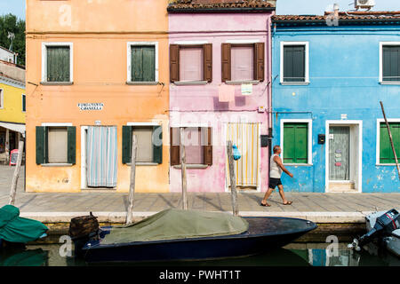 Ein Mann der Vergangenheit eine Reihe von bunten Häusern durch den Kanal in Burano, Venedig, Italien Stockfoto