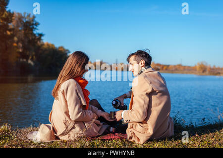 Junges Paar in Liebe Chillen bis Herbst See. Glücklich der Mann und die Frau genießen Kaffee im Freien. Die Leute trinken Kaffee auf Picknick Stockfoto