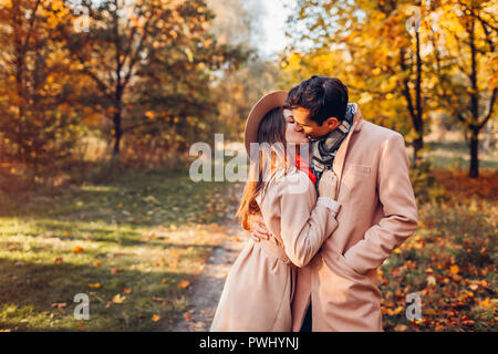 Junges Paar in Liebe Spaziergänge im Herbst Wald unter bunten Bäumen. Stilvolle Menschen umarmen und küssen bei Sonnenuntergang Stockfoto
