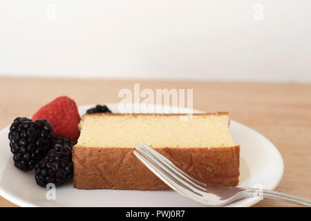 Nahaufnahme einer einzelnen Pound Cake Slice Neben einige Beeren und eine Gabel auf einem Teller für einen Snack angeordnet Stockfoto