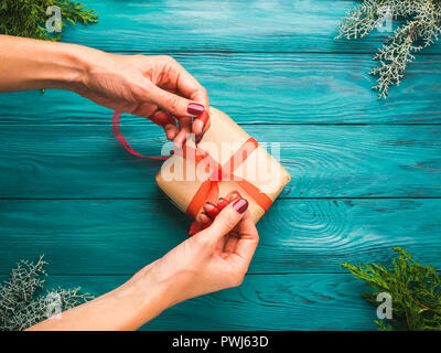 Dunkelgrün weihnachten Holz- Hintergrund mit Tannenbaum, Zweige und wickelte Geschenkbox mit roter Schleife gebunden zu sein. Strukturierte Kulisse. Die Frau Hände Stockfoto