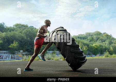 Schöne afrikanische amerikanische muskulösen Mann spiegeln große Reifen outdoor. Stockfoto