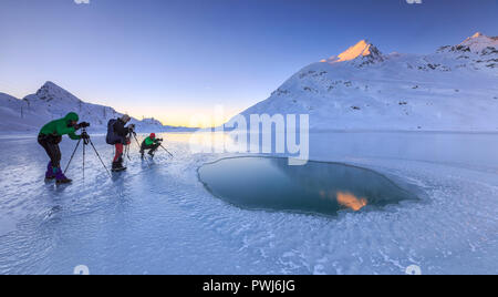 Fotografen mit Stativ am Ufer des gefrorenen Lago Bianco, Berninapass, Kanton Graubünden, Engadin, Schweiz Stockfoto