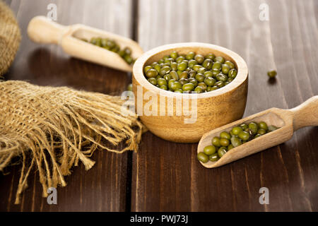 Menge ganz Trocken grüne Mungobohnen in zwei Schaufeln mit Houten auf braunem Holz Stockfoto