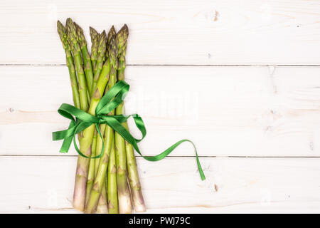 Bündel von viel von ganzen frischen grünen Spargel Speer gebunden von Green Ribbon flatlay auf weißem Holz Stockfoto