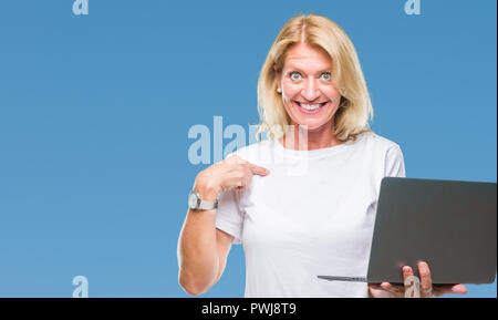 Mittleres Alter blonde Frau mit Computer Laptop über isolierte Hintergrund mit Überraschung Gesicht zeigenden Finger zu sich selbst Stockfoto