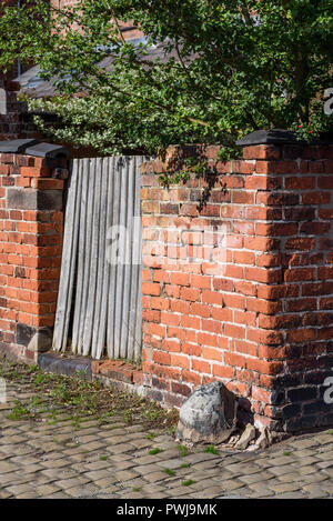 Ecke eines traditionellen britischen Viktorianisches Gasse mit alten Mauer, Tor und Kopfsteinpflaster. Stockfoto