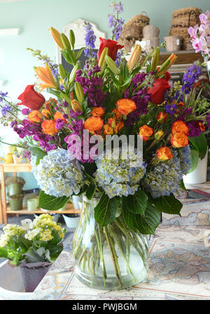 Foto von einem üppigen Blumenschmuck in einem klaren Glas Vase. Hortensien, Rosen, Lilien, Rosen, Lagerbestand, Rittersporn, etc. Stockfoto