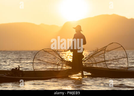 Die burmesische Fischer auf Bambus Boot, Fische zu fangen, die in traditioneller Weise mit handgefertigten net. bei Sonnenuntergang. Inle See, Myanmar (Birma) Reiseziel Stockfoto